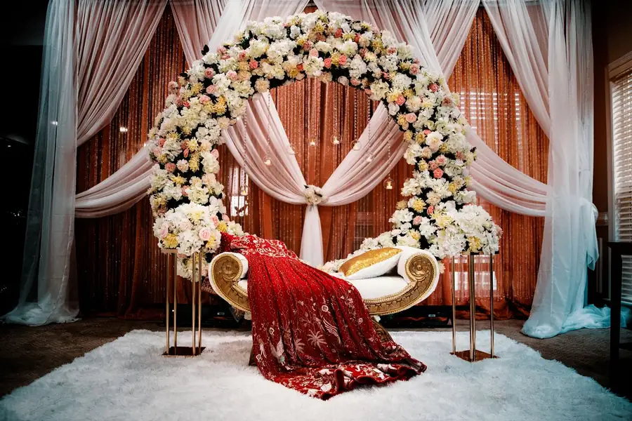 Arche fleurie de mariage devant des voilages, banquette dorée drapée de rouge