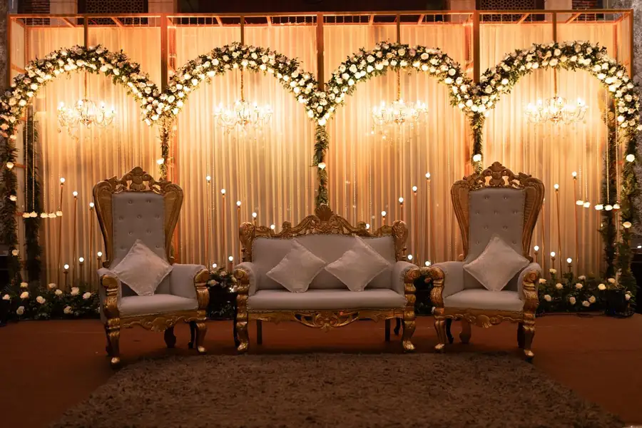 Estrade de mariage aux fauteuils dorés devant un rideau de lumières et d'arches fleuries