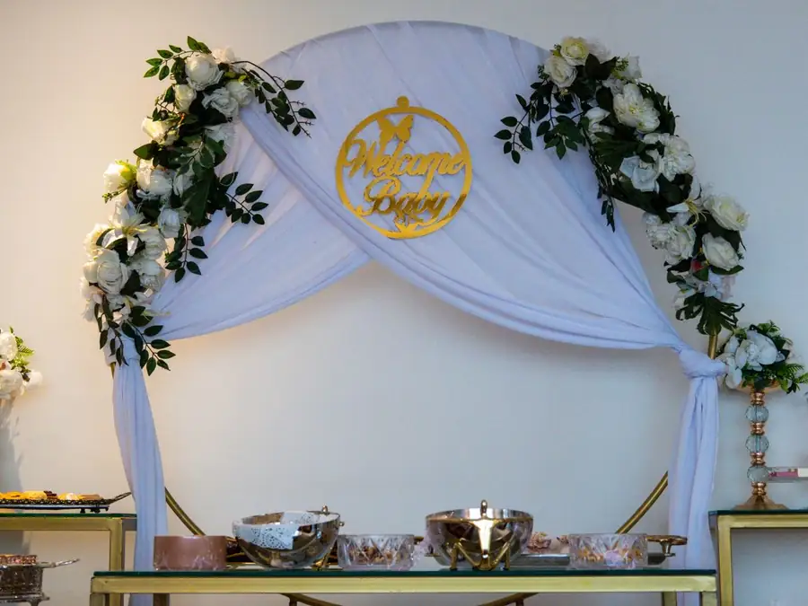 Arche de voilage blanc ornée de fleurs, avec une table de douceurs pour un baptême